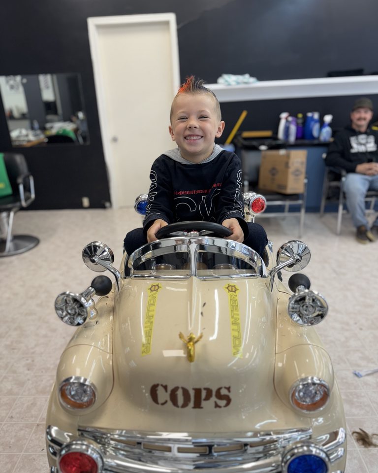 A child smiling in the shop’s car barber chair