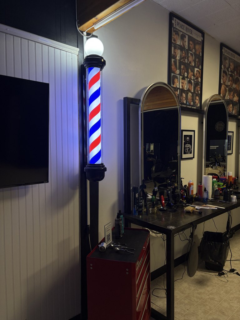 The illuminated red, white and blue barber pole beside the shop mirrors